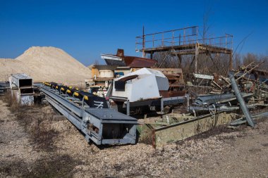 Çakıl taşı çıkarmak için kullanılan çeşitli paslı makinelerden oluşan bir grup. Arka planda çakıl yığını var. Parlak mavi gökyüzü. Puste Ulany, Slovakya.