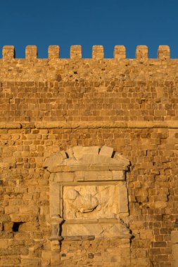 Deniz kenarındaki Venedik (Koules) kalesinin duvarının ayrıntıları. Taşların altın rengi öğleden sonra güneş ışığı altında, parlak mavi gökyüzü. Heraklion, Girit, Yunanistan.
