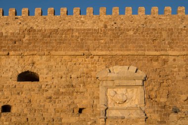 Deniz kenarındaki Venedik (Koules) kalesinin duvarının ayrıntıları. Taşların altın rengi öğleden sonra güneş ışığı altında, parlak mavi gökyüzü. Heraklion, Girit, Yunanistan.