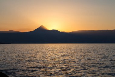 Akdeniz 'in sakin suları. Ufuktaki dağların silueti. Gün batımında gökyüzü renklidir. Heraklion, Girit, Yunanistan.