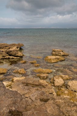 Kuzeyde bir plajın kayalık sahili. Akdeniz 'in temiz ve temiz suları. İlkbaharın başlarında bulutlu bir gökyüzü. Spiaggia (plaj) La Pelosa, Sardinya, İtalya.