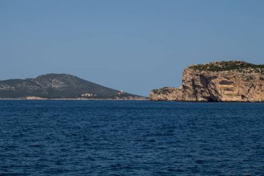 Akdeniz 'in derin mavi sularındaki bir tekneden ve ufuktaki kayalık sahilden görüntü. Doğal Park (Parco Naturale Regionale di Porto Conte), Alghero, Sardinya, İtalya 'ya yakın batı kıyısı.