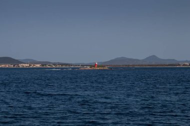 Akdeniz 'in derin mavi sularındaki bir tekneden ve ufuktaki kayalık sahilden görüntü. Doğal Park (Parco Naturale Regionale di Porto Conte), Alghero, Sardinya, İtalya 'ya yakın batı kıyısı.