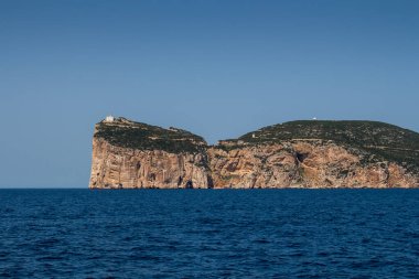 Akdeniz 'in sakin mavi suları, Capo Caccia yarımadasını çevreleyen uçurumun tepesinde beyaz bir bina. Parlak mavi gökyüzü. Sardunya, İtalya.