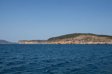 Akdeniz 'in derin mavi sularındaki bir tekneden ve ufuktaki kayalık sahilden görüntü. Doğal Park (Parco Naturale Regionale di Porto Conte), Alghero, Sardinya, İtalya 'ya yakın batı kıyısı.