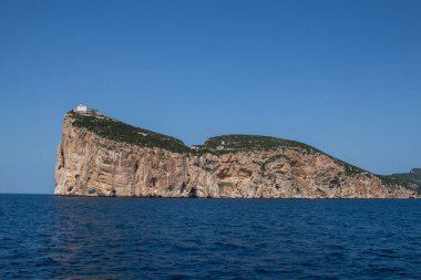 Akdeniz 'in sakin mavi suları, Capo Caccia yarımadasını çevreleyen uçurumun tepesinde beyaz bir bina. Parlak mavi gökyüzü. Sardunya, İtalya.