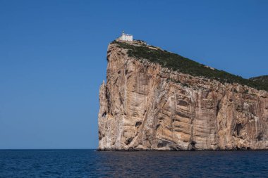 Akdeniz 'in sakin mavi suları, Capo Caccia yarımadasını çevreleyen uçurumun tepesinde beyaz bir bina. Parlak mavi gökyüzü. Sardunya, İtalya.