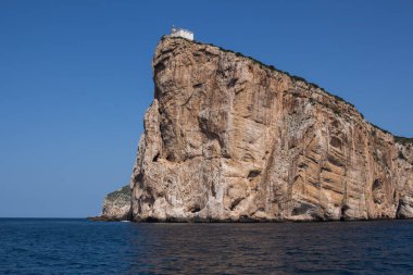 Akdeniz 'in sakin mavi suları, Capo Caccia yarımadasını çevreleyen uçurumun tepesinde beyaz bir bina. Parlak mavi gökyüzü. Sardunya, İtalya.