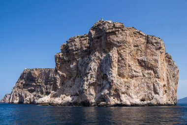 Akdeniz 'in sakin mavi suları, Capo Caccia yarımadasını çevreleyen uçurumun tepesinde beyaz bir bina. Parlak mavi gökyüzü. Sardunya, İtalya.