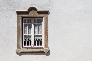 Güneşli bir günde parlak beyaz bir ev duvarı. Beyaz ahşap detayları ve eski moda perdeleri olan bir pencere. Taş çerçeveli. Estoi, Portekiz.