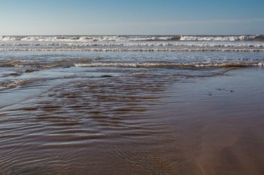 Dalgalar yükseldiğinde Atlantik Okyanusu 'nun suyu olan kumsal. Beyaz köpüklü küçük dalgalar. Parlak mavi gökyüzü. Essaouira, Fas.