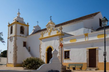 Igreja Matriz de Alvor 'un yanında, Portekiz' de bir kilisede. Sarı detaylı beyaz cephe. Parlak mavi gökyüzü. Alvor, Algarve, Portekiz.