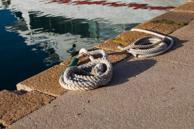 Akdeniz limanında bir spiral içine sarılmış iki beyaz güçlü ip. Arka planda su var. Güneşli bir gün. Alghero, Sardinya, İtalya.