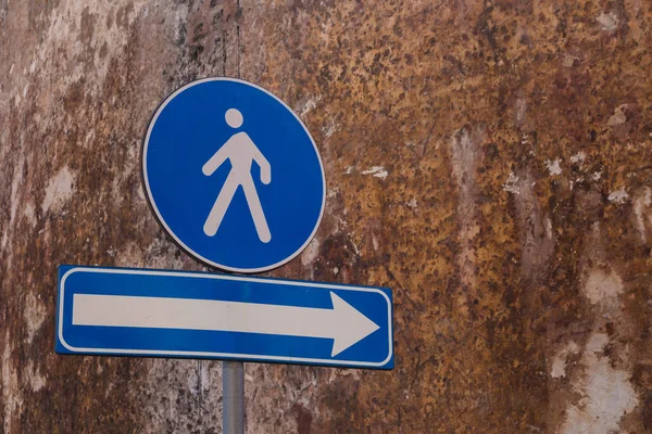 两个蓝色交通标志 一个是行人专用的 另一个是右箭头 后背一幢建筑物的旧风化石墙 Alghero Sardinia 意大利 — 图库照片