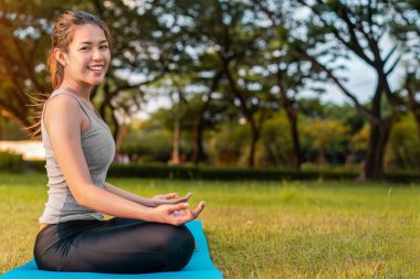 Mutlu Asyalı kadın meditasyon yapıyor ve Lotus 'ta oturuyor. Park, Sağlıklı ve Yoga Konsepti, Zihin-Vücut Geliştirme Konsepti, Seçici Odaklanma, Boşluğu Kopyalama.