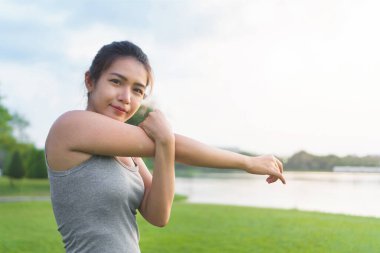Egzersiz konsepti, genç Asyalı kadın koşucu sabah koşmadan önce kolunu esnetiyor, seçici odaklanma.