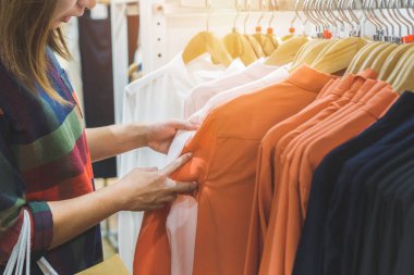 Alışveriş çantalı mutlu Asyalı kadın alışveriş merkezinde şık kıyafetler alıyor, seçici odaklı..