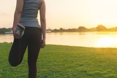 Egzersiz konsepti, genç Asyalı kadın koşucu sabah koşmadan önce kolunu ve bacağını esnetiyor, seçici bir odak noktası.