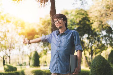 Genç Asyalı iş adamı dizüstü bilgisayarıyla çalıştıktan sonra dinleniyor ve tatilde parkta online galibiyetinin tadını çıkarıyor..