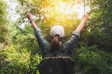 Yaz tatili konsepti, sırt çantalı Asyalı kadın gezgin ayakta duruyor ve elini tropik ormanın yakınına uzatıyor ve uzaklara bakıyor..