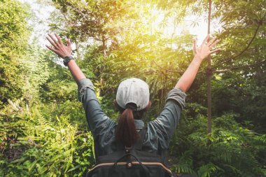 Yaz tatili konsepti, sırt çantalı Asyalı kadın gezgin tropikal ormanın yanında duruyor ve uzaklara bakıyor..