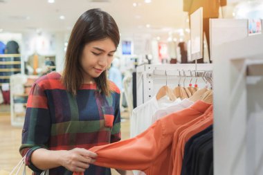 Alışveriş torbalarıyla alışveriş yapan mutlu genç Asyalı kadın alışveriş merkezinde moda giysiler, seçici odaklanma.