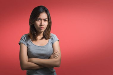 Duygusal konsept, kırmızı arka planda gri elbiseli kameraya bakarak kollarını kavuşturmuş kızgın, sevimli Asyalı kadının portresi..