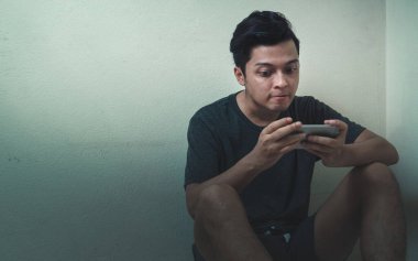 Kızgın Asyalı adam akıllı telefonuyla düşük ışık ortamı ile mobil oyun oynuyor..