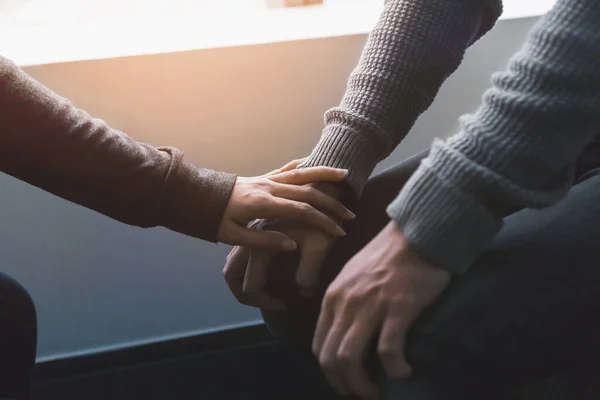 Travma sonrası stres bozukluğu, zihinsel sağlık konsepti, psikolog oturuyor ve pencerenin yanında düşük aydınlık çevreye sahip genç Asyalı adamı cesaretlendirmek için el ele tutuşuyor..