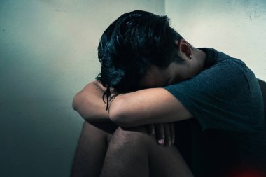 Genç bunalımlı Asyalı adam karanlık odada yalnız başına oturuyor. Düşük ışık ortamı, seçici odaklanma, travma sonrası stres bozukluğu zihinsel sağlık konsepti..