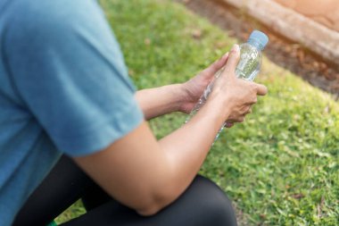 Genç Asyalı kadın koşucu, sabah spordan sonra elinde içme suyu şişesiyle parkta bankta oturuyor. Egzersiz ve sağlıklı bir konsept..