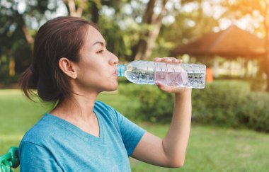 Egzersiz ve sağlıklı konsept, genç Asyalı kadın koşucu spordan sonra sabah erken saatlerde parkta açık havada içme suyu içiyor..