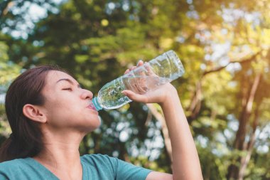 Genç Asyalı kadın koşucu sabahın erken saatlerinde spor sonrası parkta şişede içme suyunu rahatlatıyor. Egzersiz ve sağlıklı bir konsept.,
