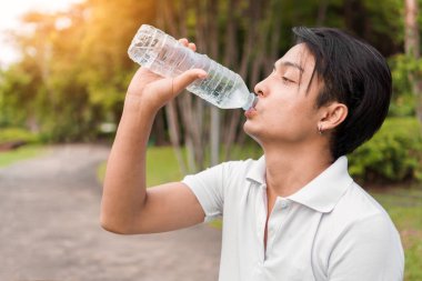 Genç Asyalı koşucu sabahın erken saatlerinde spor sonrası parkta şişede içme suyunu rahatlatıyor, egzersiz ve sağlıklı bir konsept..
