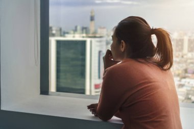 Travma sonrası stres bozukluğu, depresyonda olan Asyalı bir kadın sabahları pencerenin yanında tek başına oturuyor..