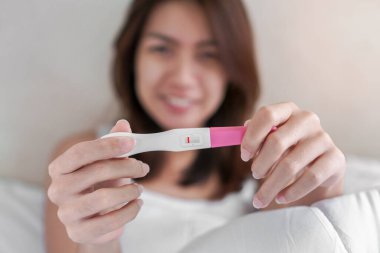 Mutlu genç Asyalı kadın gülümsüyor ve hamilelik testi yapıyor ve yatak odasında negatif sonuçlar almaktan mutlu, sağlıklı konsept, kürtaj sorunu, seçici odaklanma sorunu.