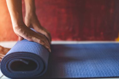 Genç Asyalı kadın oturma odasında mavi yoga minderi ya da spor minderi yuvarlıyor, sağlıklı konsept, zihin-vücut geliştirme konsepti.