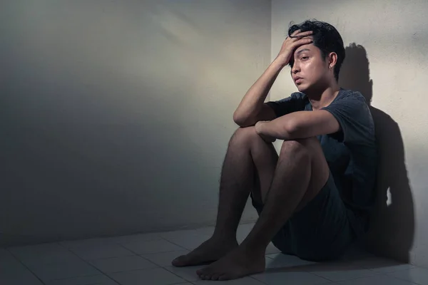Travma sonrası stres bozukluğu, depresyondaki Asyalı genç adam, karanlık bir odada, düşük aydınlık bir ortamda, seçici bir odak noktasında oturuyor..