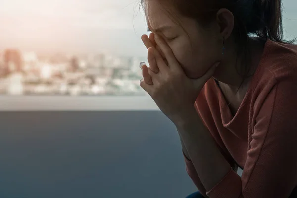 Genç depresif Asyalı kadın akşam vakti pencerenin kenarında yalnız başına oturuyor. Düşük ışık ortamı, travma sonrası stres bozukluğu, zihinsel sağlık, seçici odaklanma....