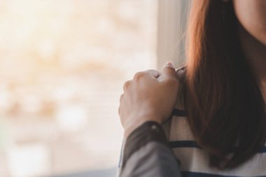 Psikolog, düşük ışık ortamı, seçici odaklanma, PTSD Akıl Sağlığı Konsepti ile pencerenin yakınındaki depresif Asyalı genç kadına dokunuyor..
