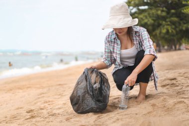 Asyalı bir kadın şişeyi plastik torbaya doldurup sabahları plajı temizlemek için siyaha boyuyor. Gönüllü konsepti..