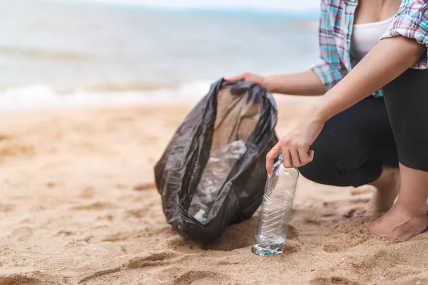 Asyalı bir kadın şişeyi plastik torbaya doldurup sabahları plajı temizlemek için siyaha boyuyor. Gönüllü konsepti..