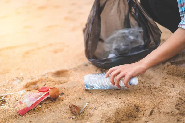 Asyalı bir kadın şişeyi plastik torbaya doldurup sabahları plajı temizlemek için siyaha boyuyor. Gönüllü konsepti..