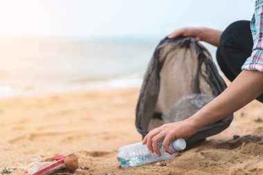 Asyalı bir kadın şişeyi plastik torbaya doldurup sabahları plajı temizlemek için siyaha boyuyor. Gönüllü konsepti..