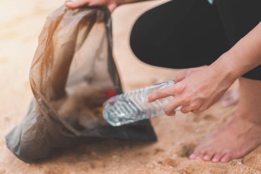 Asyalı bir kadın şişeyi plastik torbaya doldurup sabahları plajı temizlemek için siyaha boyuyor. Gönüllü konsepti..