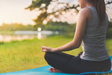 Asyalı kadın meditasyon yapıyor ve lotusta oturuyor. Parkta poz veriyor, Sağlıklı ve Yoga Kavramı, Zihin-Vücut Geliştirme Konsepti, Seçici Odaklanma, Boşluğu Kopyalama.