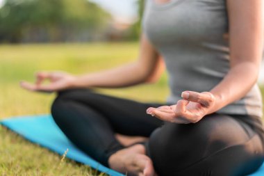 Asyalı kadın meditasyon yapıyor ve lotusta oturuyor. Parkta poz veriyor, Sağlıklı ve Yoga Kavramı, Zihin-Vücut Geliştirme Konsepti, Seçici Odaklanma, Boşluğu Kopyalama.