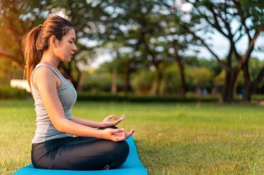 Asyalı kadın meditasyon yapıyor ve lotusta oturuyor. Parkta poz veriyor, Sağlıklı ve Yoga Kavramı, Zihin-Vücut Geliştirme Konsepti, Seçici Odaklanma, Boşluğu Kopyalama.