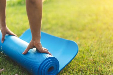 Asyalı genç bir kadın mavi yoga minderi ya da spor minderi yuvarlıyor. Park, sağlıklı konsept ve zihin-vücut geliştirme konseptinde egzersiz yapmaya hazır olun..