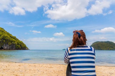 Güzel mavi gökyüzü olan tropikal kumlu plajda oturan Asyalı kadının arkadan görünüşü.